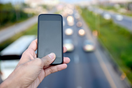 Hand holding smartphone against background many car driving on road