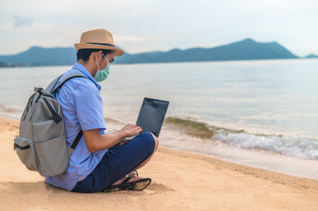 Man wear mask using laptop computer on beach  sea  and Man travel holiday Phuket sandbox Thailand...