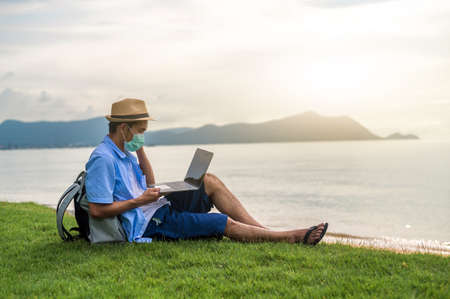 Man wear mask using laptop computer on beach  sea  and Man travel holiday Phuket sandbox Thailand are freedom life financialの写真素材