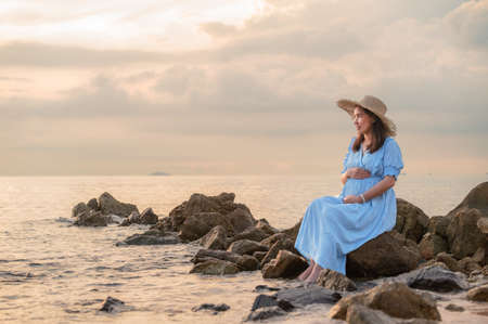 pregnant woman sitting the rocks near the sand beach and the sea.の写真素材