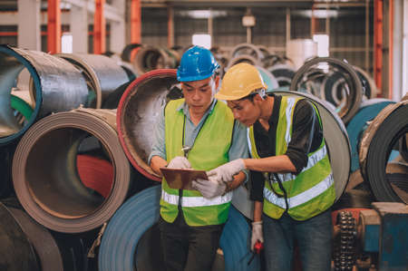 Asian engineer factory manager and mechanic worker employee in safety hard hat talking and inspection inside the factoryの写真素材