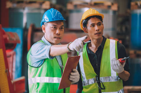 Asian engineer factory manager and mechanic worker employee in safety hard hat talking and inspection inside the factoryの写真素材