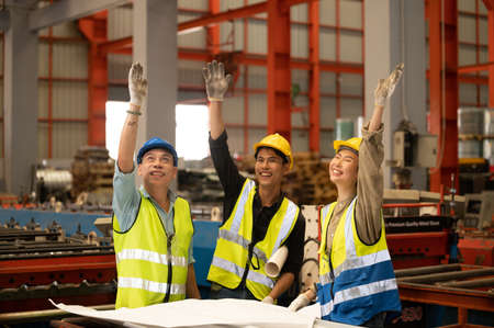 Teamwork co-workers Technicians and Engineer workers with hardhat or helmet, vest showing hands coordination and raising fist smiling for successful working in workplace of industry Factoryの写真素材