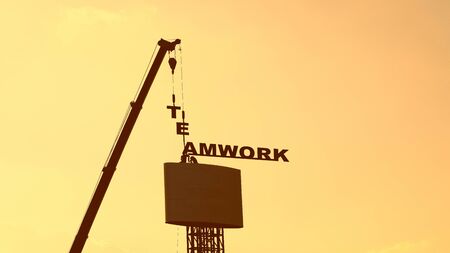 Workers and cranes are installing "TEAMWORK" text billboard, sunset sky.の写真素材