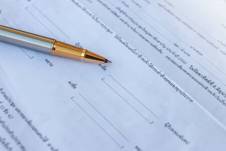 Low angle view of golden pen lying on white sheet of paper in a folder with another set of paperworkの写真素材