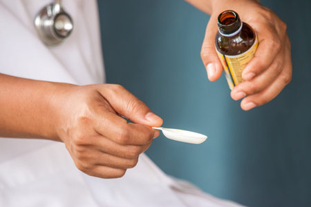healthcare, treatment and medicine concept - bottle of medication or antipyretic syrup and spoon