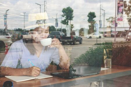 Asian woman wearing hat working on laptop in coffee shop.の写真素材