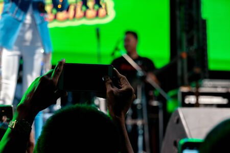 People use mobile phones to live or take pictures at concerts, with bright lights at night.の写真素材