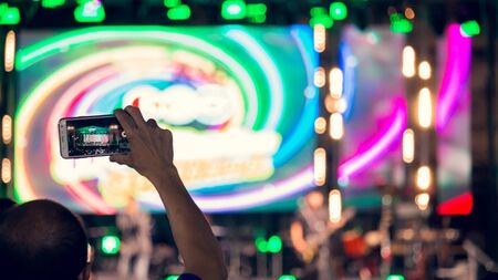 People use mobile phones to live or take pictures at concerts, with bright lights at night.の写真素材
