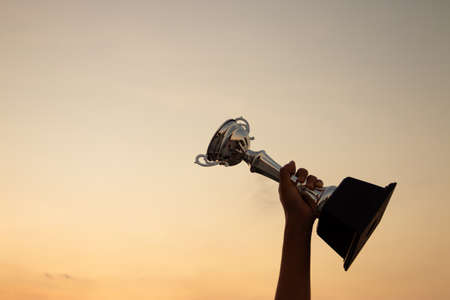 Victory concept with a hand holding a trophy on the sunset sky backgroundの写真素材