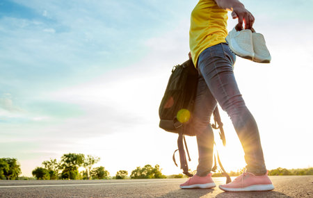 The woman left the work shoes and wore sneakers on the highway with the golden light of the sun. Concept of vacation and travelの写真素材