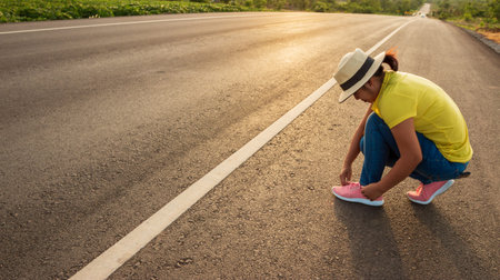 Women tourists tying the sneakers on the highway with the golden light of the sun, backpacker concept.の写真素材