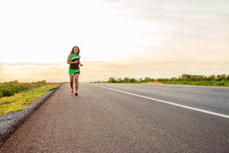 Along the road in the hillside area at the time of the sun set woman is exercising by running.の写真素材