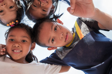 Low angle shot of excited children stand in circle hugging looking at camera at playing together, Team of smiling kids embracing together in a circle. Portrait of young boy and girls looking at camera, Friendship conceptのeditorial素材