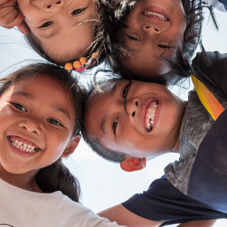 Low angle shot of excited children stand in circle hugging looking at camera at playing together, Team of smiling kids embracing together in a circle. Portrait of young boy and girls looking at camera, Friendship conceptのeditorial素材