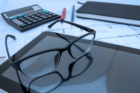 Architect desk with construction plans, tablet, glasses at architect studioの写真素材