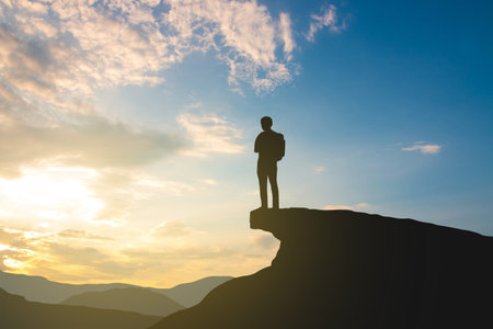 silhouette of backpacker on mountain top over sky and sun light background,business, success, leadership, achievement and people conceptの写真素材