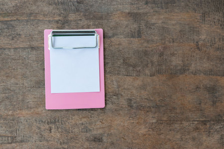 Small pink clipboards with a blank sheet of paper on wooden backgroundの写真素材