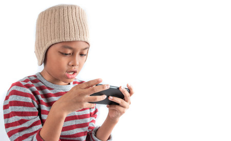 Little asian boy in wool hat using smart phone on white backgroundの写真素材