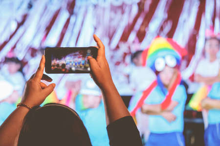 Parents use their phones to take pictures of their children on stage at school.の写真素材