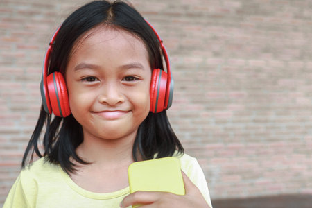 A cute Asian girl uses a red wireless headphone to listen to music on her phone.