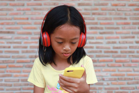 A cute Asian girl uses a red wireless headphone to listen to music on her phone.の写真素材