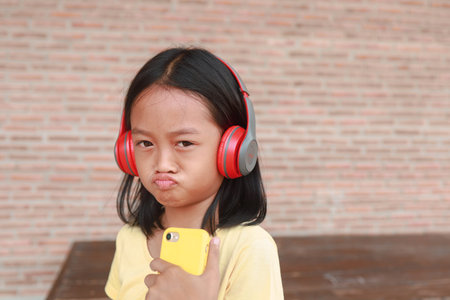 A cute Asian girl uses a red wireless headphone to listen to music on her phone.