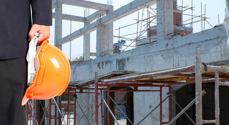 Engineer holding an orange safety hat on the background of the construction site