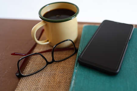 Yellow coffee mugs, phones and books on the wooden table inside the house.の写真素材