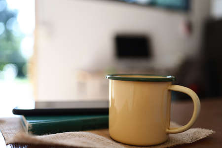 Yellow coffee mugs, phones and books on the wooden table inside the house.の写真素材