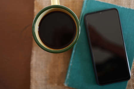 Yellow coffee mugs, phones and books on the wooden table inside the house.の写真素材