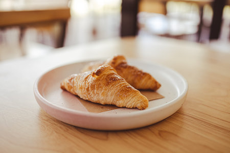 Two appetizing croissants on a plate are placed on a wooden table in the cafe.
