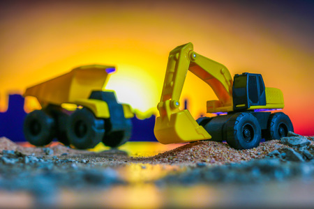 Construction engineering concept , Excavator machine toy and Truck toy working on construction field with silhouette sunset backgroundの写真素材