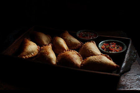 Freshly Baked Empanadas Arranged in a Semi-Circle with Vibrant Chimichurri Sauce on a Black Backgroundの写真素材