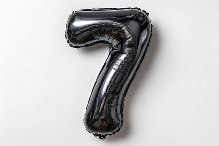 A shiny black foil balloon shaped like the number 7 is positioned vertically against a plain white...