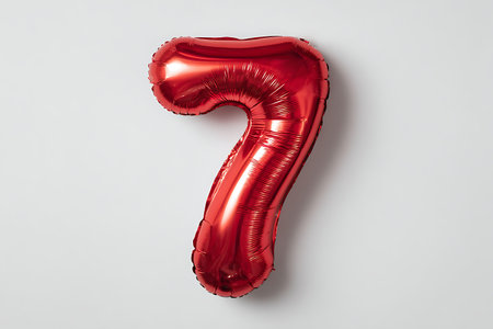 A bright red, metallic foil balloon in the shape of the number seven is displayed on a plain white background. The surface of the balloon reflects light, creating highlights and shadows that emphasize its rounded form and the texture of the foil. The image is a studio shot of a single party decoration.の写真素材