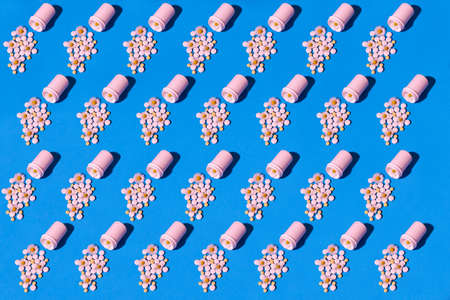A pattern of white and yellow pills spilling out of a jar on a blue background with chamomile flowers.の写真素材