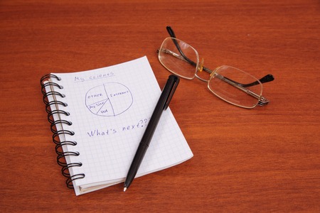 ballpoint pen, glasses and an open notebook lying on the tableの写真素材