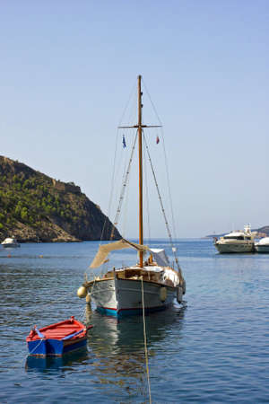 sailing boat sail rolled anchored off close to a rowing boatの写真素材