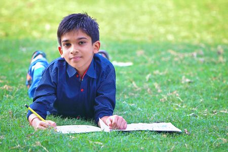 Portrait of Indian little boy is drawing, lying down on green grassの写真素材