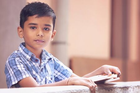 Portrait of Indian little boy posing to camera with school text bookの写真素材