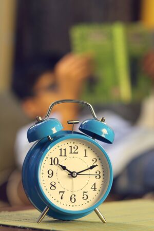 Indian young boy sleeping with textbook and alarm is in front of himの写真素材
