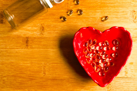 Vitamin D3 gel capsules in a small red heart bowl on a wooden top.の写真素材