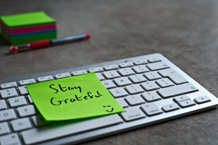 Stay Grateful green sticky note left on keyboard. The bright note stands out against the keys,...