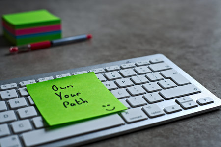 Own Your Path green sticky note left on keyboard. The bright note stands out against the keys,...