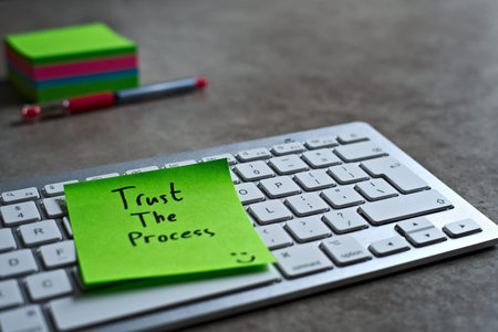 Trust The Process green sticky note left on keyboard. The bright note stands out against the keys,...