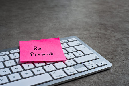 Be Present sticky note left on keyboard. The bright note stands out against the keys, symbolising...