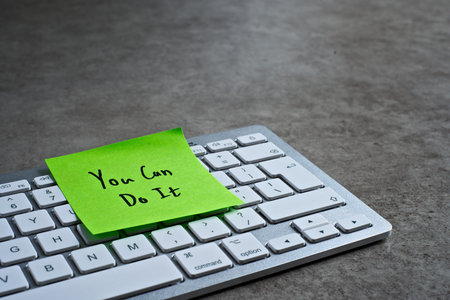 You Can Do It sticky note left on keyboard. The bright note stands out against the keys, symbolising...