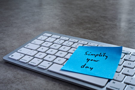 Simplify your day sticky note left on keyboard. The bright note stands out against the keys,...