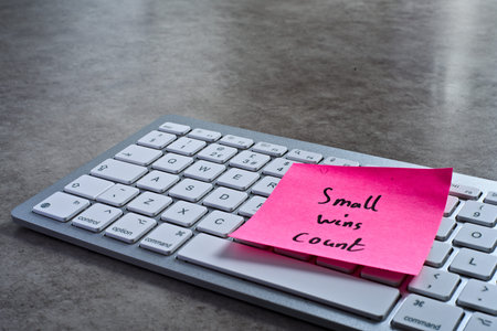 Small wins count sticky note left on keyboard. The bright note stands out against the keys,...